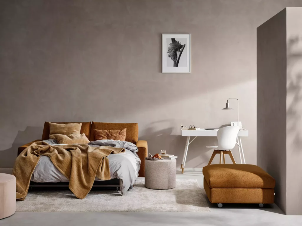 Meble modułowe w salonie w stylu skandynawskim – brązowa sofa z funkcją spania, biurko i jasne minimalistyczne wnętrze