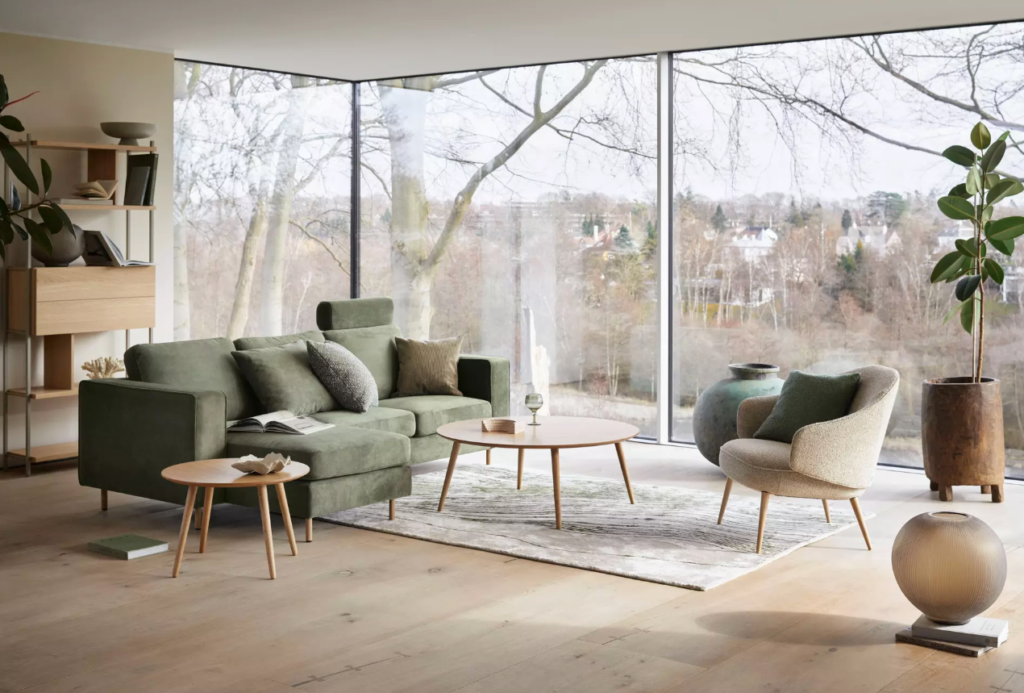 Zielona sofa narożna w nowoczesnym salonie z dużymi przeszkleniami i skandynawskim wystrojem