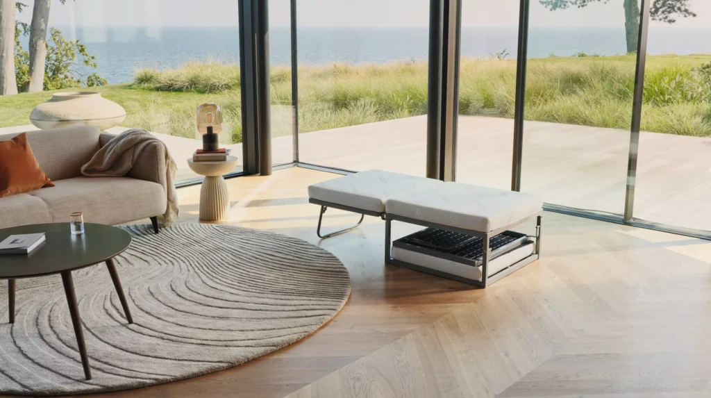 Pufa Xtra BoConcept podczas rozkładania do funkcji spania. Zdjęcie pokazuje zintegrowany mechanizm, który pozwala przekształcić kompaktową pufę w wygodne łóżko dla gości.