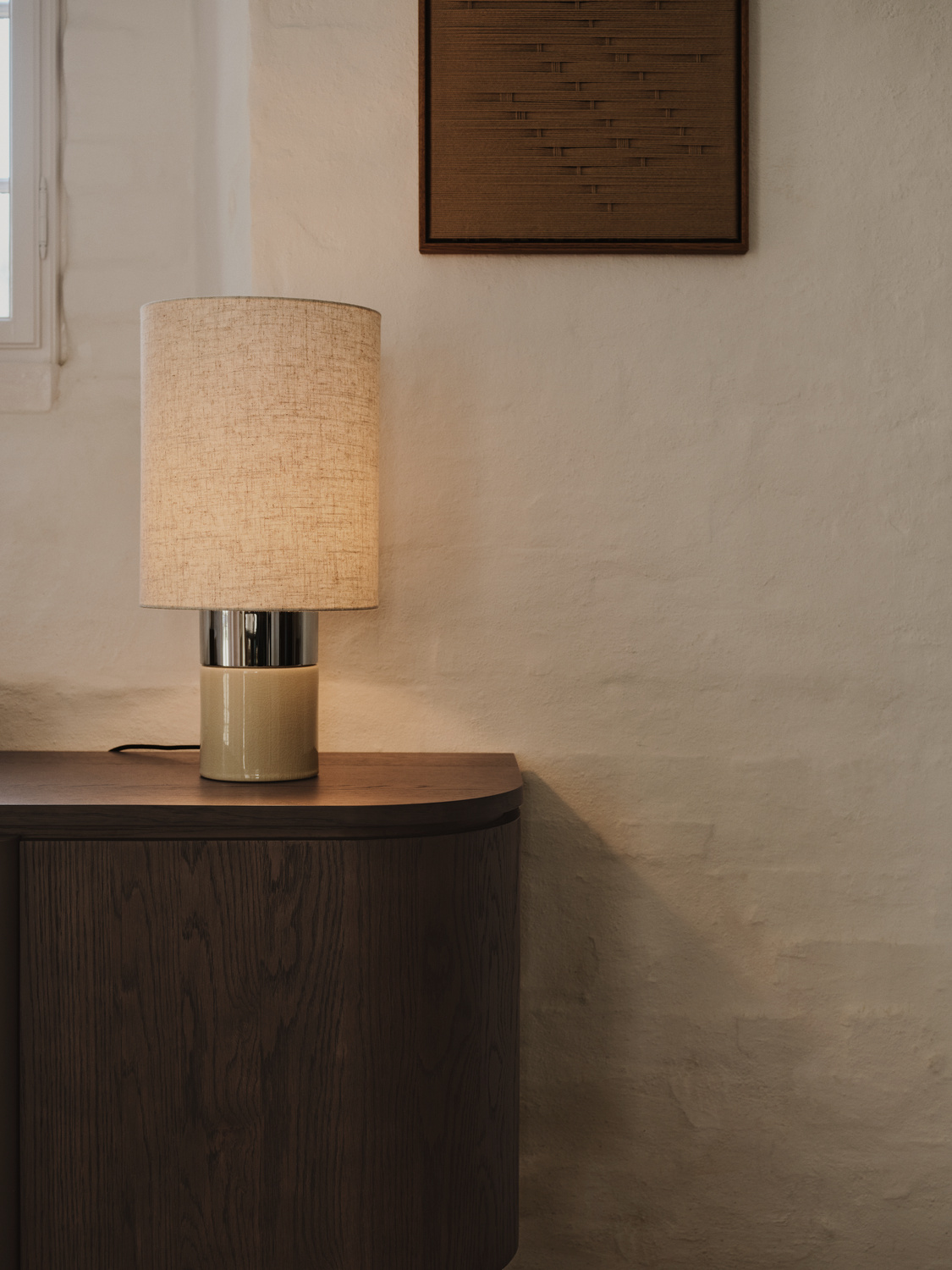 Nastrojowo oświetlona lampa stołowa BoConcept na ciemnym drewnianym meblu